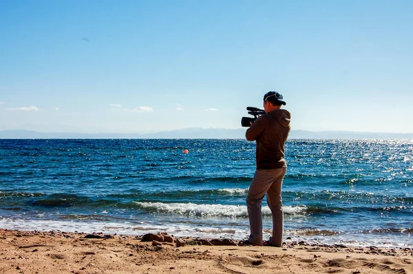 A man shoots video on a video camera on the background of the sea