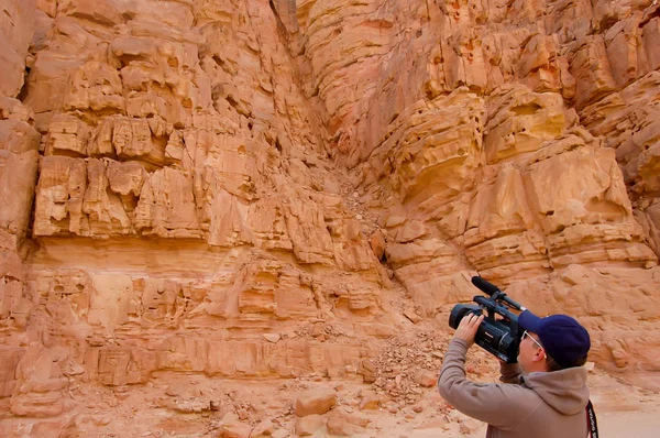 a man shoots video on a video camera against a stone red mountain