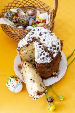 Siyah ve beyaz çikolata sosu, bahar çiçekleri ve parlak sarı masa örtüsü, arkasında bir Paskalya sepeti üzerinde yumurta Paskalya kek