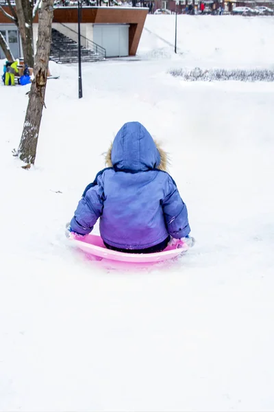 在粉红色的冰屋上穿蓝色夹克的婴儿从山上下来 — 图库照片