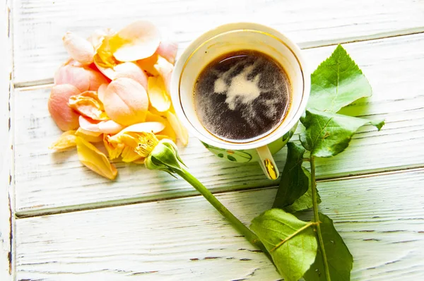 cup of coffee with rose petals on light wooden background