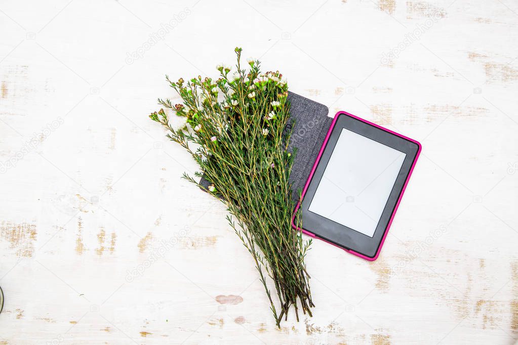 There is an open e-book on a white, worn background, with wild flowers on it.