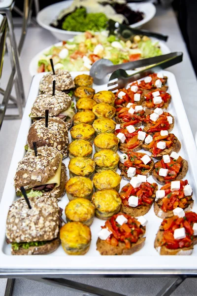 bruschetta on grilled bread with cottage cheese and vegetables ratatouille, quiche loren with chicken and cheese mini burger with veal pastry, cheese, mustard sauce and cucumber at catering event on some festive event, party or wedding reception