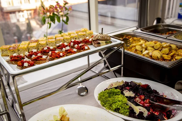 bruschetta on grilled bread with soft cheese and vegetable ratatouille, quiche loren and a mini burger with fried mackerel, tartar sauce, fresh cucumber and ice salad and salates at catering event on some festive event, party or wedding reception