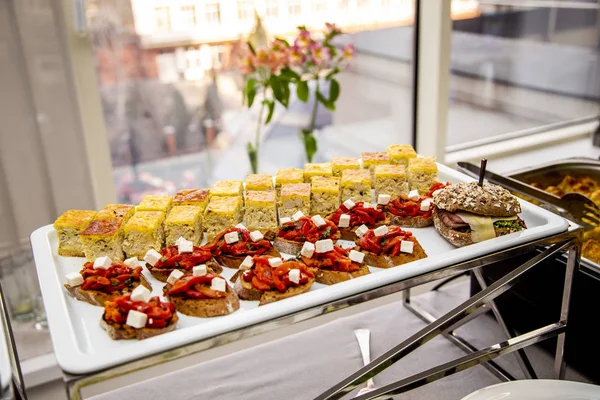 bruschetta on grilled bread with soft cheese and vegetable ratatouille, quiche loren and a mini burger with fried mackerel, tartar sauce, fresh cucumber and ice salad. at catering event on some festive event, party or wedding reception