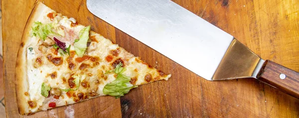 piece of pizza (from mozzarella, chicken, bacon, pommdor, salad mix) on wood