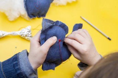 Bir ders ya da bir dikiş Atölyesi - çocuk elleri sarı tablo üzerinde koyu mavi kumaş oyuncak dikmek