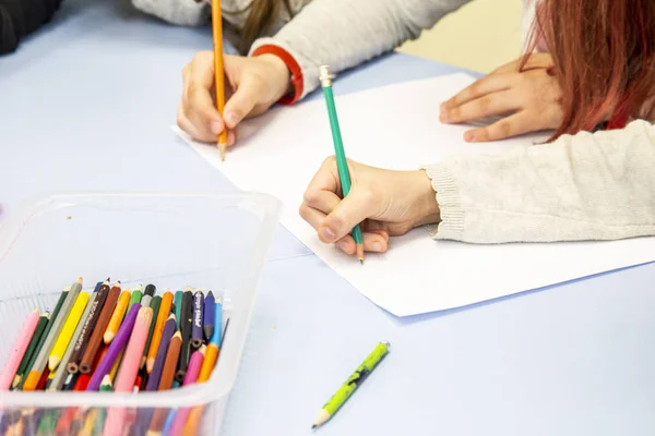 hands of two children draw with pencils on one sheet of paper