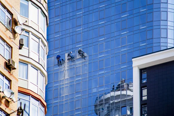 3 men wash mirrored windows at high, Urban modern construction and dangerous occupation