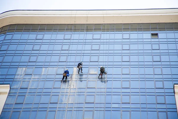 3 men wash mirrored windows at high, Urban modern construction and dangerous occupation