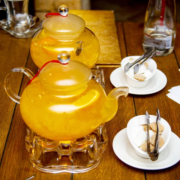 2 colheres de chá de espinheiro do mar e chá de laranja em queimadores de chá, açúcar branco e marrom em discos brancos ao lado de uma mesa de madeira em um café ou restaurante — Fotografia de Stock