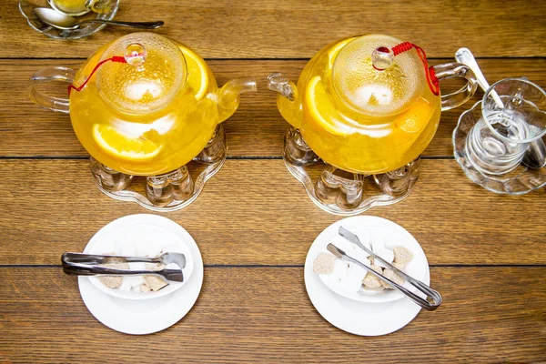 2 чайные ложки облепихи и апельсинового чая стоят на чайных горелках, белый и коричневый сахар на белых тарелках рядом с деревянным столом в кафе или ресторане — стоковое фото