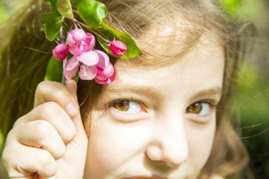 neşeli küçük kız güneşli bir günde kafasına bir çiçek açan kiraz ağacının bir dalı koymak, bir sly bakmak