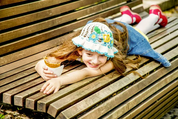 Vrolijke meid met roomijs in haar hand ligt een houten bankje op een zonnige dag — Stockfoto