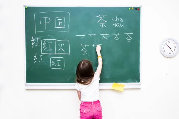 A menina perto da diretoria da escola escreve caracteres chineses — Fotografia de Stock