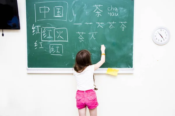 A menina perto da diretoria da escola escreve caracteres chineses — Fotografia de Stock