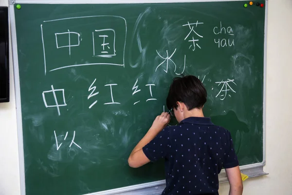 Pojken i närheten av skolstyrelsen skriver kinesiska tecken — Stockfoto