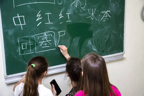 O professor e as crianças perto do conselho escolar escreve caracteres chineses — Fotografia de Stock