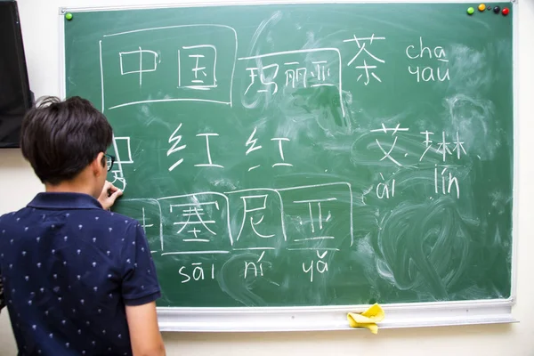 Pojken i närheten av skolstyrelsen skriver kinesiska tecken — Stockfoto