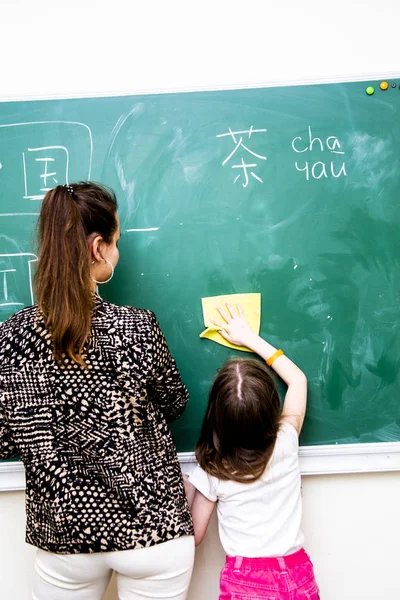 Flicka och lärare våtservetter en grön skola styrelse från kinesiska tecken — Stockfoto