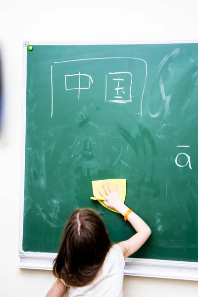 Menina limpa uma placa de escola verde de caracteres chineses — Fotografia de Stock