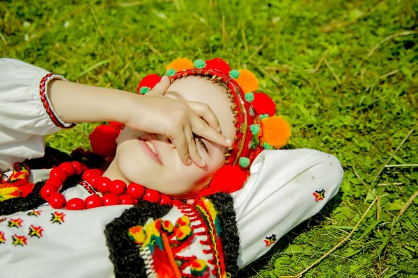 Menina em um velho traje ucraniano nacional encontra-se na grama verde em um dia ensolarado — Fotografia de Stock