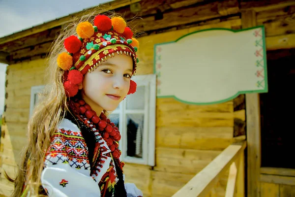 Портрет красивой девушки в старом национальном украинском костюме на фоне горно-зеленого пейзажа и деревянного дома в солнечный день — стоковое фото