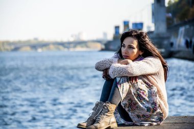 Koyu renk saçlı, açık renk kazaklı bir kadın sonbaharda denize bakıyor.