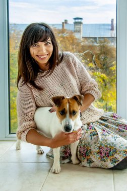 Koyu renk saçlı güzel bir kadın yerde köpek cinsi Jack Russell 'la oturuyor, sonbahar havasında.