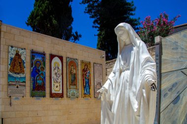 NAZARETH, ISRAEL, 26 Haziran 2020: Bakire Meryem 'in heykeli İsrail, Nasıra' daki Annunciation Bazilikası 'nın avlusunda. Duvarın yanında farklı ülkelerden gönderilen Bakire Meryem 'i gösteren renkli paneller var.