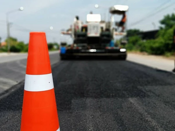 Road maintenance by the ASPHALT HOT MIX IN - PLACE RECYCLING method and with a red cone in the front (blurred image).