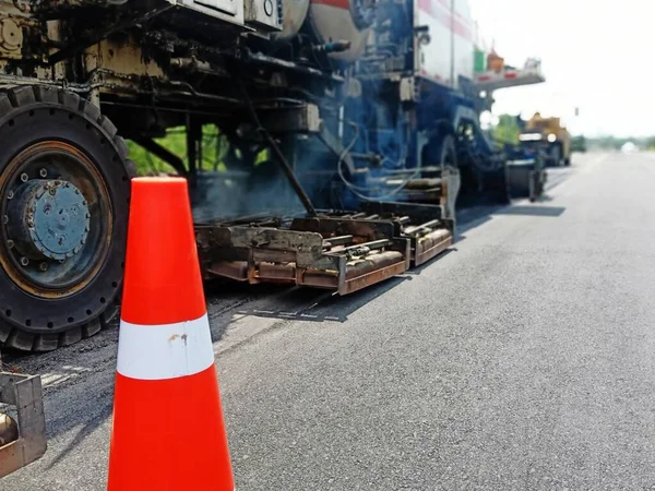 Road maintenance by the ASPHALT HOT MIX IN - PLACE RECYCLING method and with a red cone in the front (blurred image).