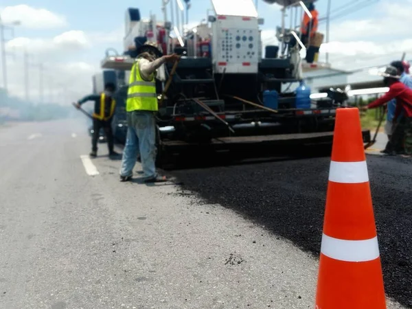 Road maintenance by the ASPHALT HOT MIX IN - PLACE RECYCLING method and with a red cone in the front (blurred image).