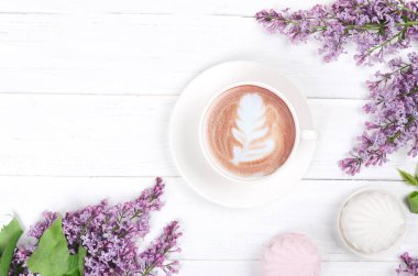 Leylak, latte resimli kahve ve beyaz ahşap masada beyaz ve pembe marşmelov. Romantik bir sabah. Düz yatıyordu