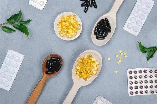 Black and yellow pills and wooden spoon on gray background — Stock Photo, Image