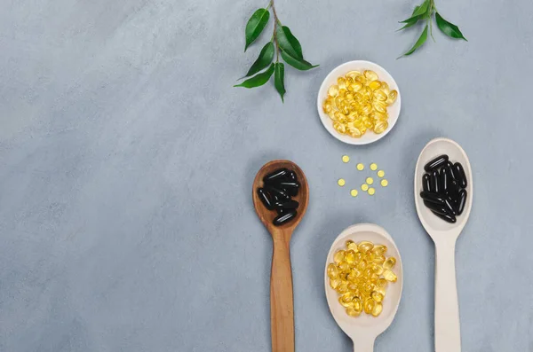 Black and yellow pills on wooden spoon on gray background — Stock Photo, Image