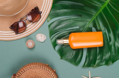 Yaz hasır şapkası, tropikal canavar yaprağı, güneş gözlüğü, kabuk, güneş kremi, yeşil arka planda deniz yıldızı..