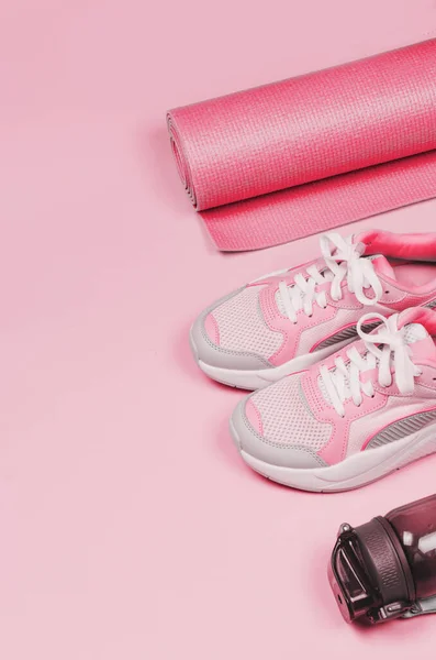 Yoga mat, sport shoes, bottle of water on pink background. Healthy lifestyle