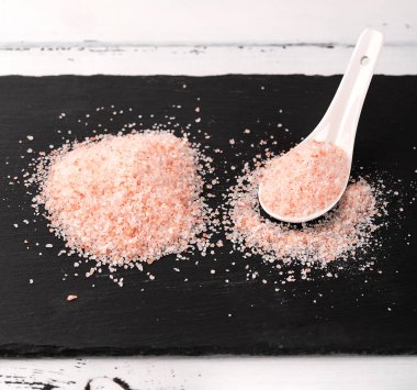 Siyah taş zemin üzerine seramik kaşık pembe Himalaya tuzu.