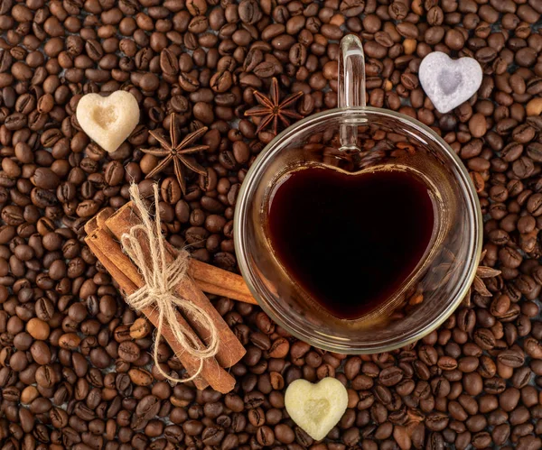 Coffee cup in the shape of heart on coffee beans with sinnamon and anise background. Top view
