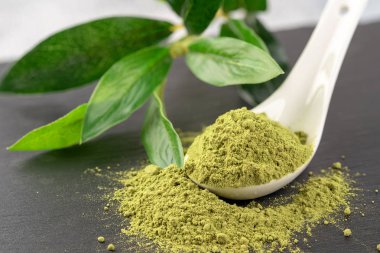 Matcha toz beyaz seramik kaşık ve siyah arka plan üzerine çay yaprakları