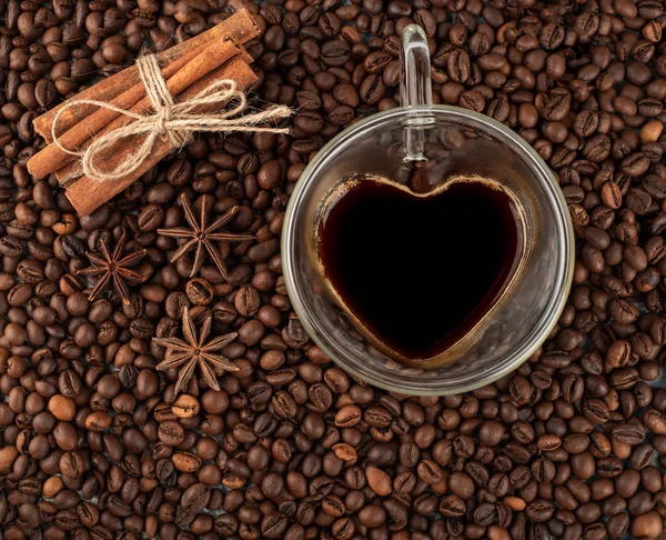 Coffee cup in the shape of heart on coffee beans with cinnamon and anise background. Top view