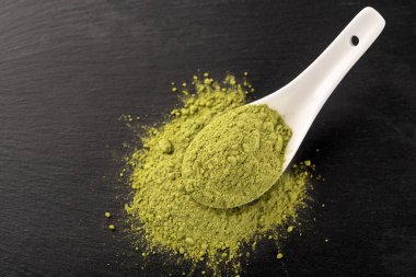 Matcha toz beyaz seramik kaşık ve siyah arka plan üzerine çay yaprakları