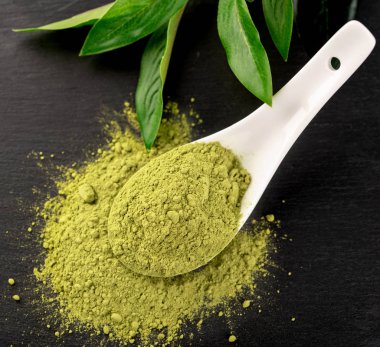 Matcha toz beyaz seramik kaşık ve siyah arka plan üzerine çay yaprakları