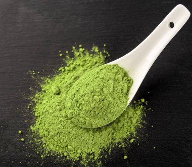 Matcha toz beyaz seramik kaşık ve siyah arka plan üzerine çay yaprakları