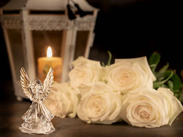 Glass angel with fallen feathers, roses and candle on a dark background