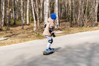 Çocuk ilkbaharın başlarında parkta kaykay sürüyor. fro'su görüntüle