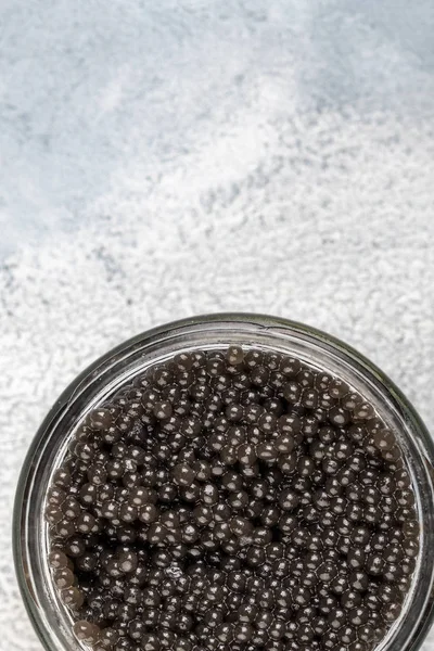 Zwarte kaviaar in een glazen pot op een lichte achtergrond — Stockfoto