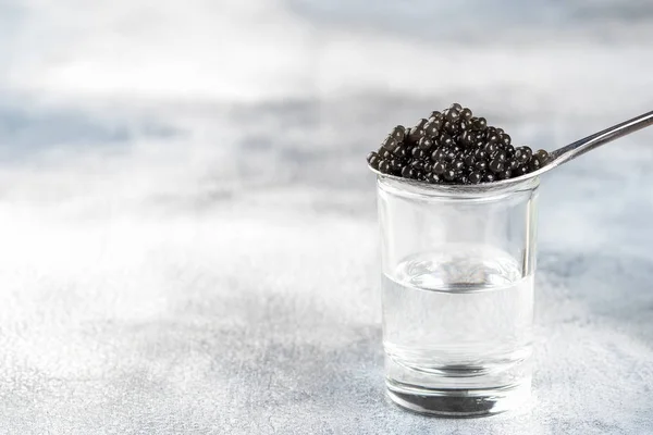 Cucchiaio d'argento di caviale nero e vetro di vodka su backgro leggero — Foto Stock