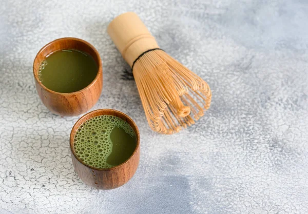 Matcha green tea in a wooden cups and bamboo whisk on light stone table. High quality photo
